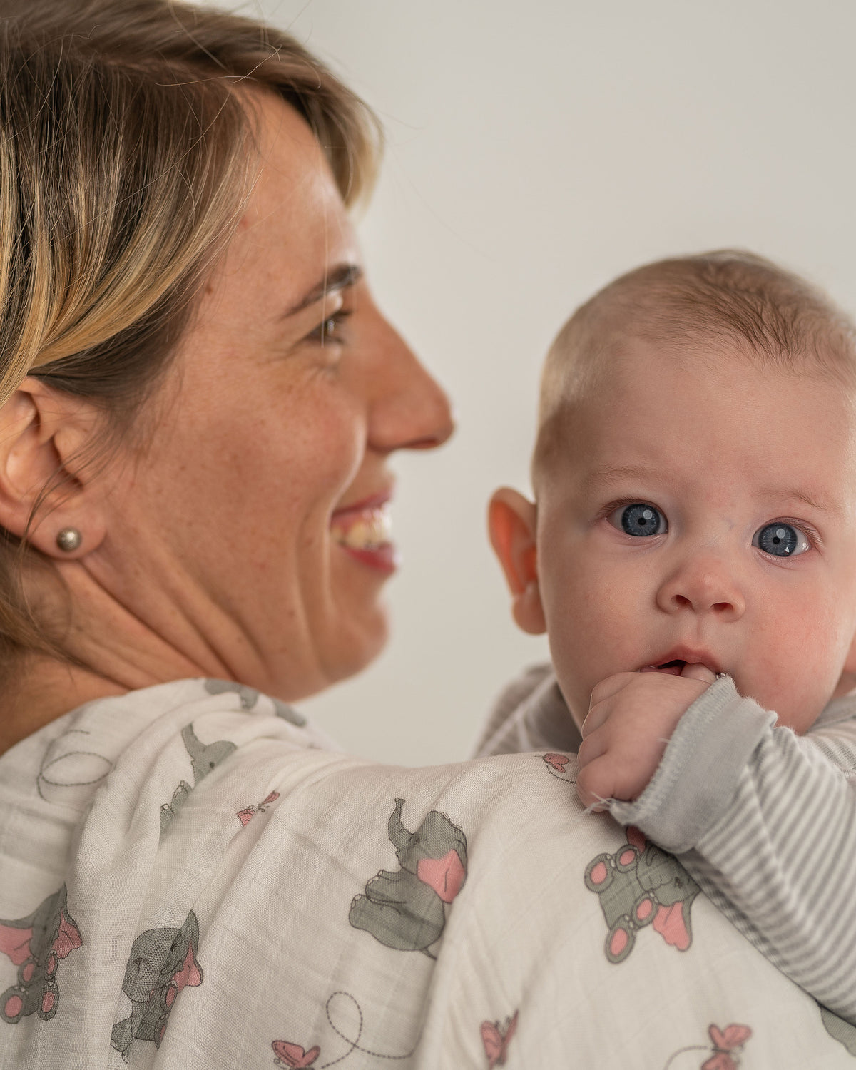 Mutter hält ihr Baby auf dem Arm, über der Schulter eine Tabalino Mullwindel Rosa Elefanten