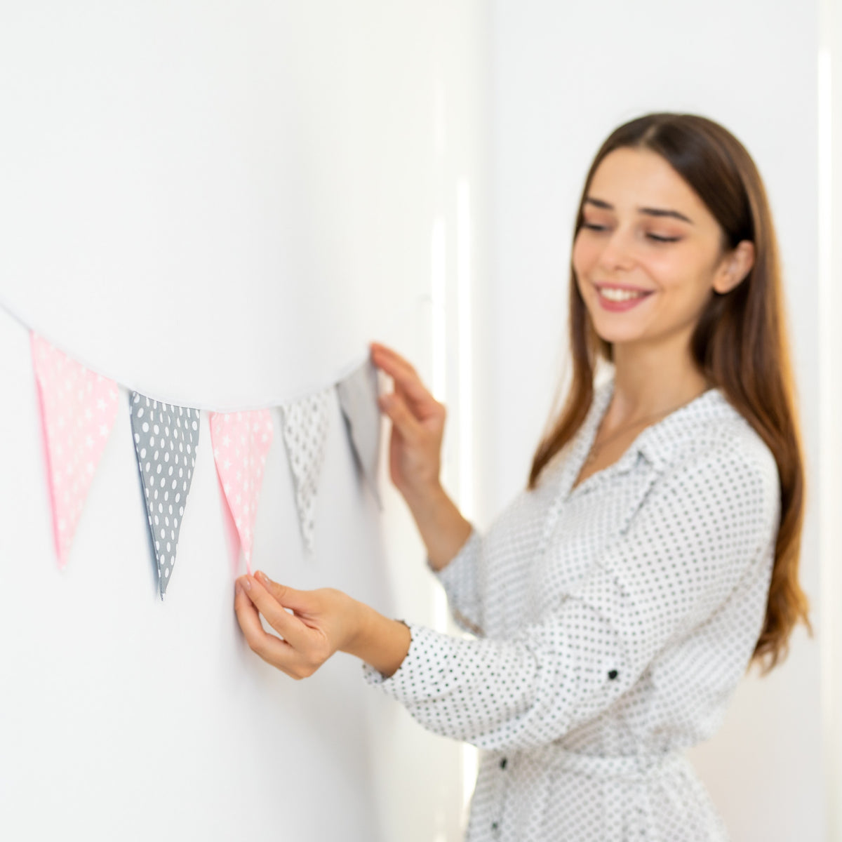Frau hängt eine Wimpelkette in Rosa und Grau an die Wand