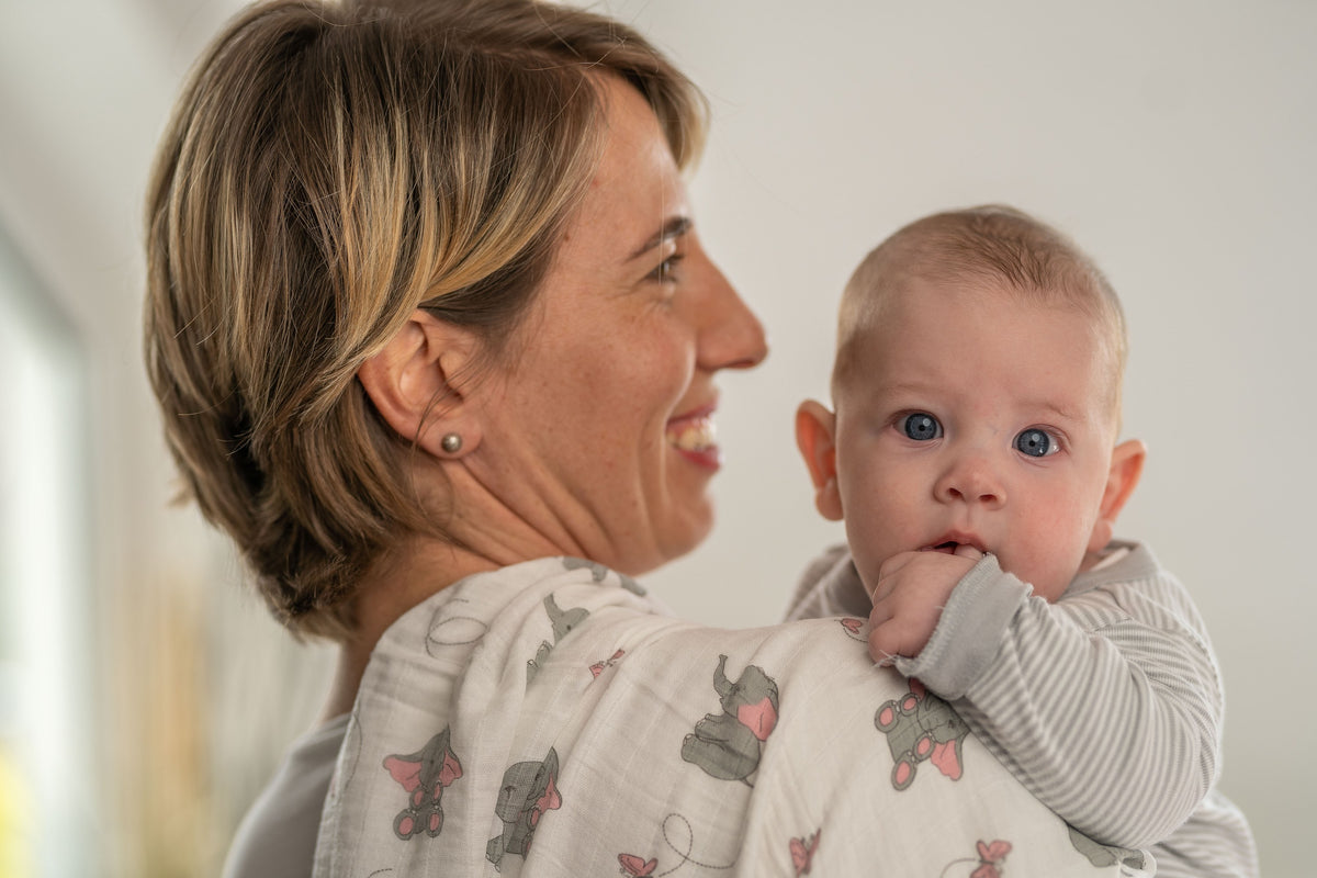 Mutter hält ihr Baby auf dem Arm, über der Schulter eine Tabalino Mullwindel mit Elefanten-Muster
