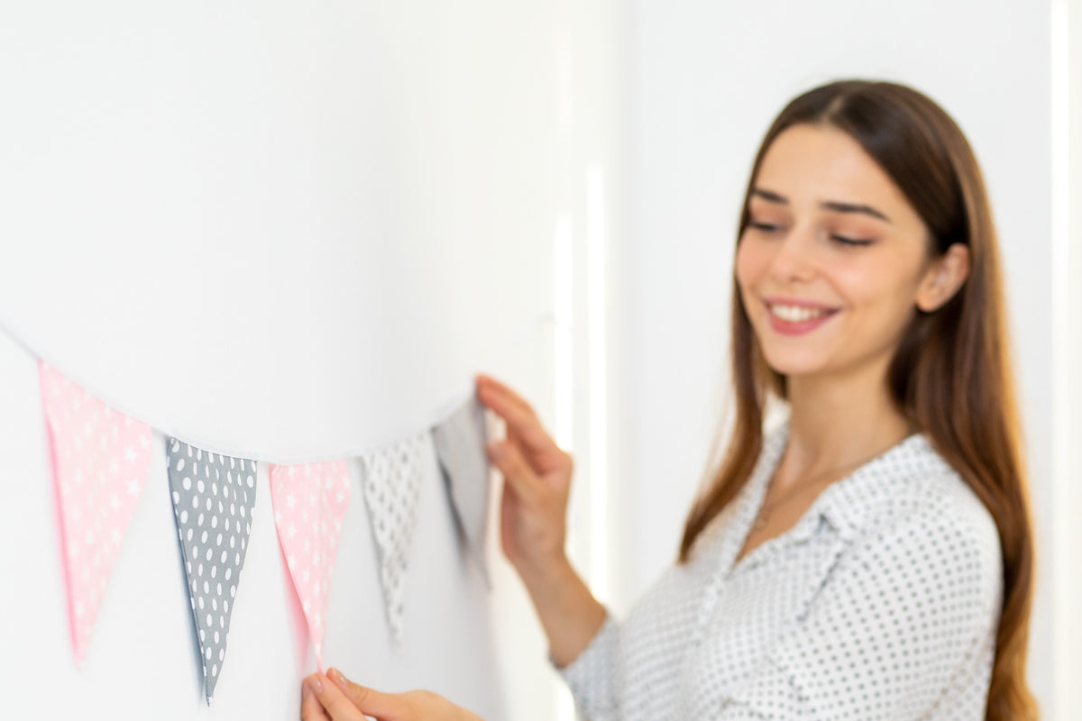 Frau hängt eine Wimpelkette in Rosa und Grau an eine weiße Wand