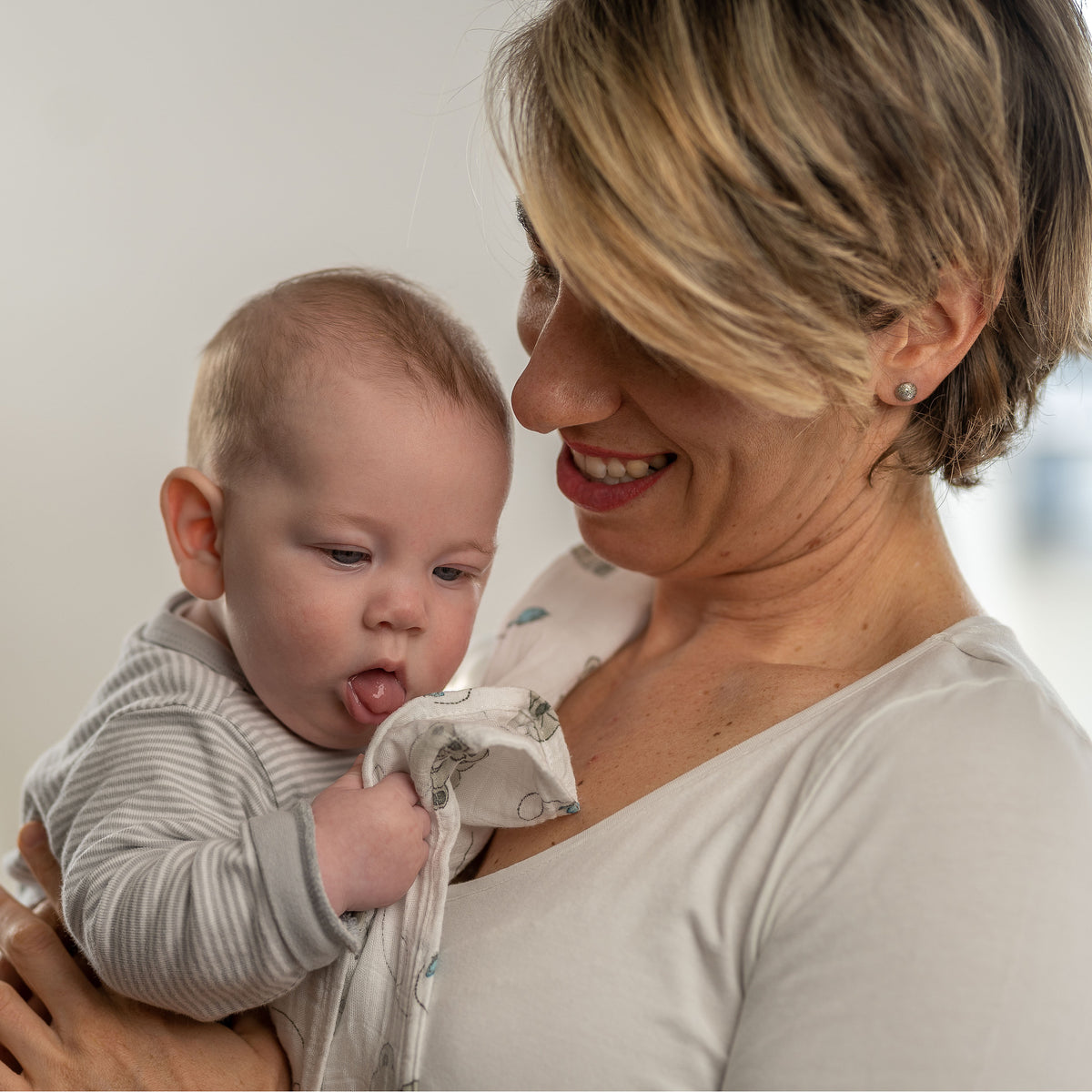 Mutter hält ihr Baby auf dem Arm, über der Schulter eine Tabalino Mullwindel Teddy & Wolken